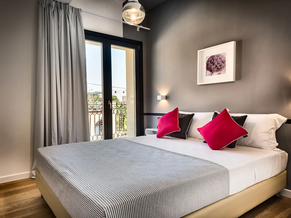 Teku Boutique Hotel a Bari Sardo – l’Ogliastra più autentica Camera da letto con letto matrimoniale, cuscini rosa e porte-finestre sul balcone