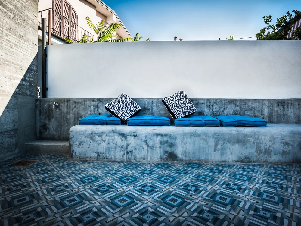 Teku Boutique Hotel a Bari Sardo – l’Ogliastra più autentica Terrazza con panca in cemento, cuscini blu e pavimento a mosaico geometrico