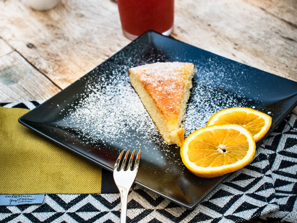 Teku Boutique Hotel a Bari Sardo – l’Ogliastra più autentica Fetta di torta spolverata di zucchero a velo con fette d’arancia, succhi e frutta fresca