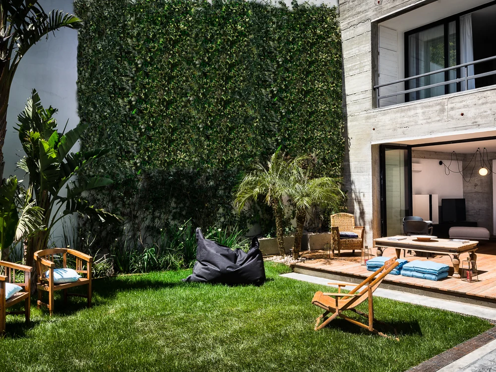 Teku Boutique Hotel a Bari Sardo – l’Ogliastra più autentica Giardino con prato, piante tropicali e sedute accanto a una moderna casa in cemento