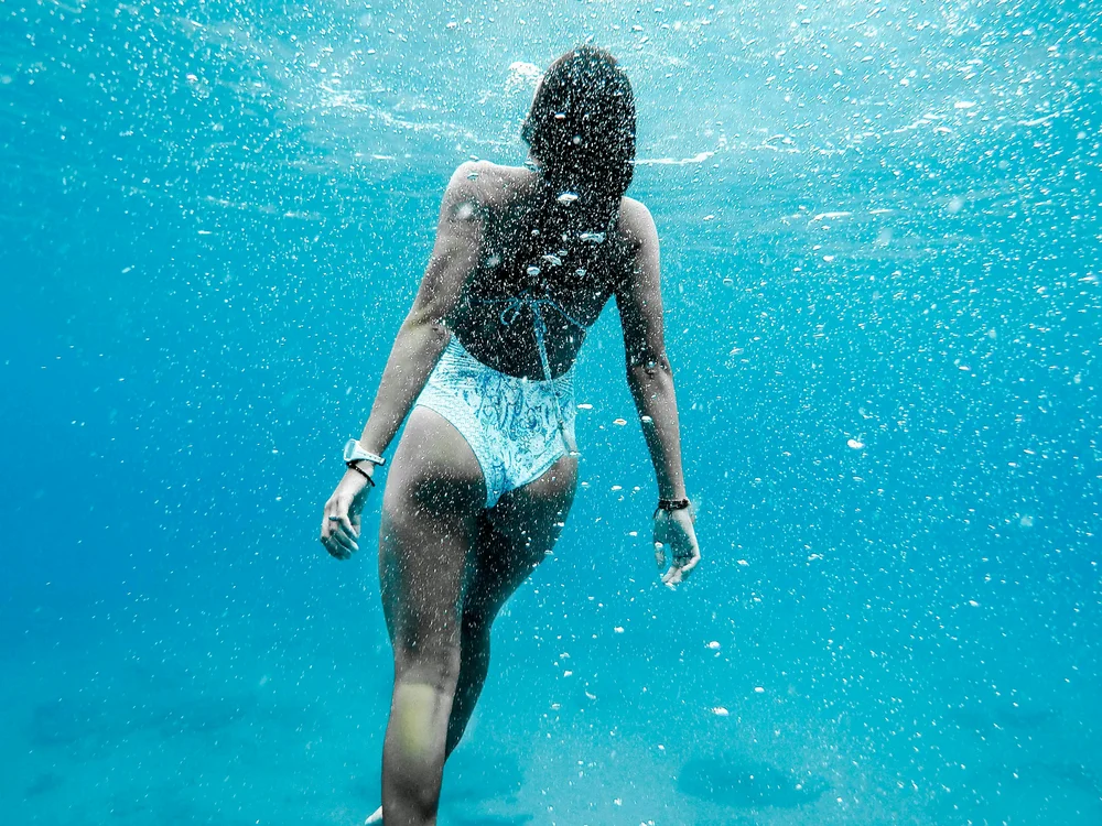Teku Boutique Hotel a Bari Sardo – l’Ogliastra più autentica Donna in costume nuota sott’acqua tra bolle nel mare turchese