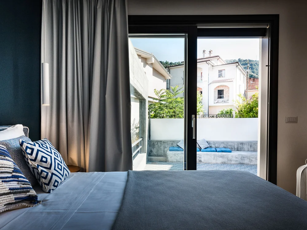 Teku Boutique Hotel a Bari Sardo – l’Ogliastra più autentica Camera da letto con letto matrimoniale e porte vetrate che si aprono su un patio