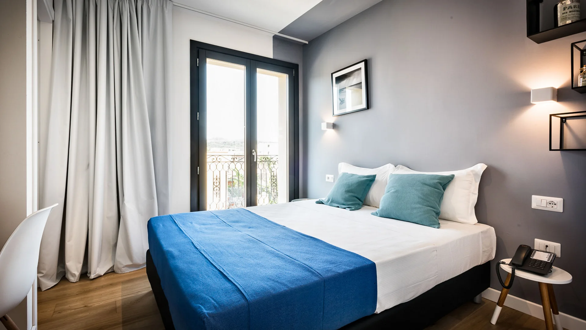 Camera moderna con letto matrimoniale, coperta blu e porte a vetri sul balcone