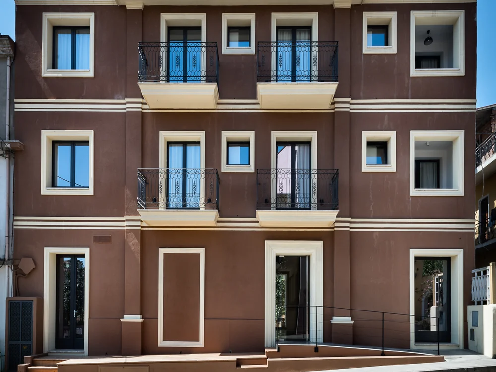 Teku Boutique Hotel a Bari Sardo – l’Ogliastra più autentica Facciata di un edificio marrone a tre piani con balconi e finiture color crema